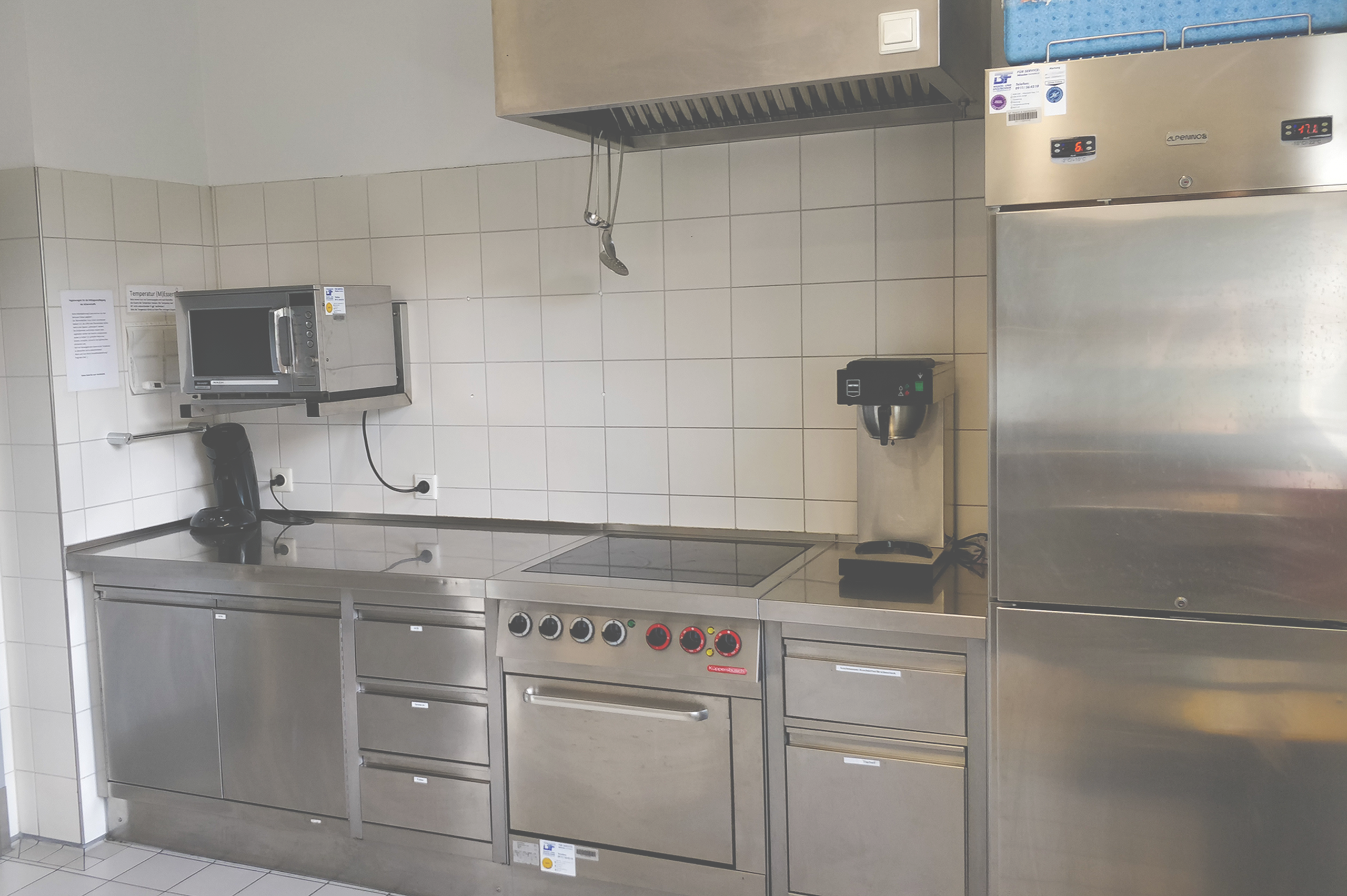Foto der Industrieküche mit Kühlschrank, Herd, Ofen, Mikrowelle und Küchenschränken aus Metall-